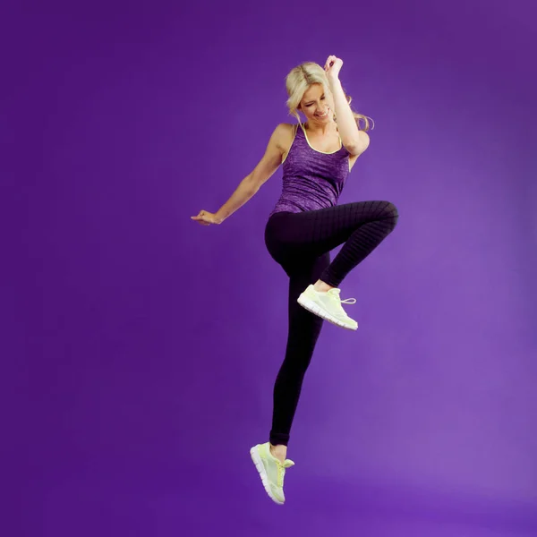 Hermosa joven en un corredor de pose. Fondo del estudio, morado. Feliz salto. — Foto de Stock