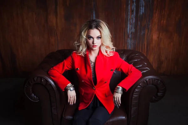Νέοι και ελκυστική ξανθιά γυναίκα στο κόκκινο σακάκι κάθεται σε δερμάτινη πολυθρόνα, τοίχος φόντο grunge σκουριασμένο — Φωτογραφία Αρχείου