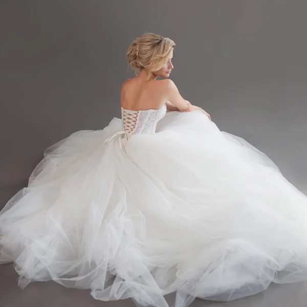 Charmante junge Braut im luxuriösen Hochzeitskleid. hübsches Mädchen in Weiß. grauer Hintergrund. zurück — Stockfoto