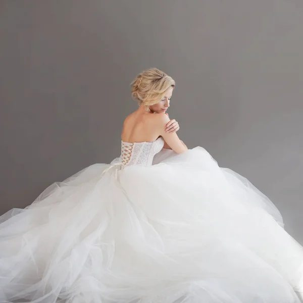 Charmante junge Braut im luxuriösen Hochzeitskleid. hübsches Mädchen in Weiß. grauer Hintergrund. zurück — Stockfoto