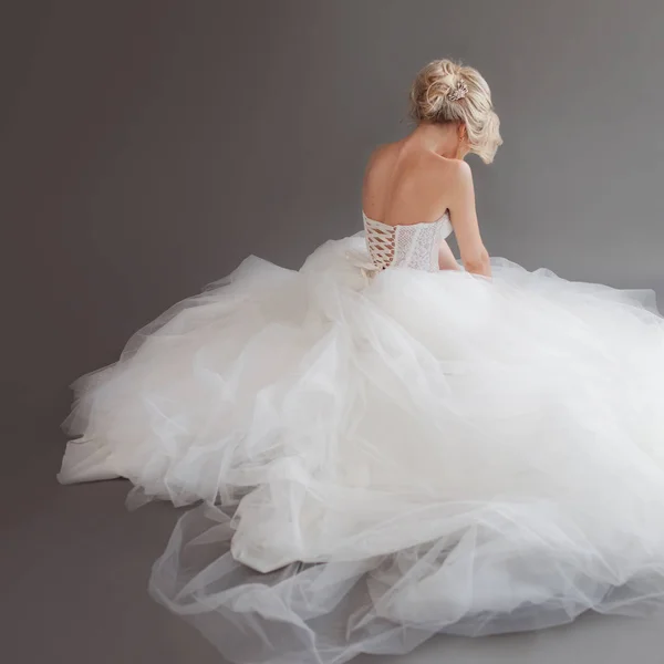Jovem noiva encantadora em vestido de casamento luxuoso. Menina bonita de branco. Fundo cinzento. Para trás. — Fotografia de Stock