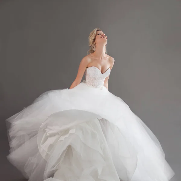 Dançando noiva jovem em vestido de noiva de luxo. Menina bonita de branco. Emoções de felicidade, riso e sorriso, fundo cinza — Fotografia de Stock