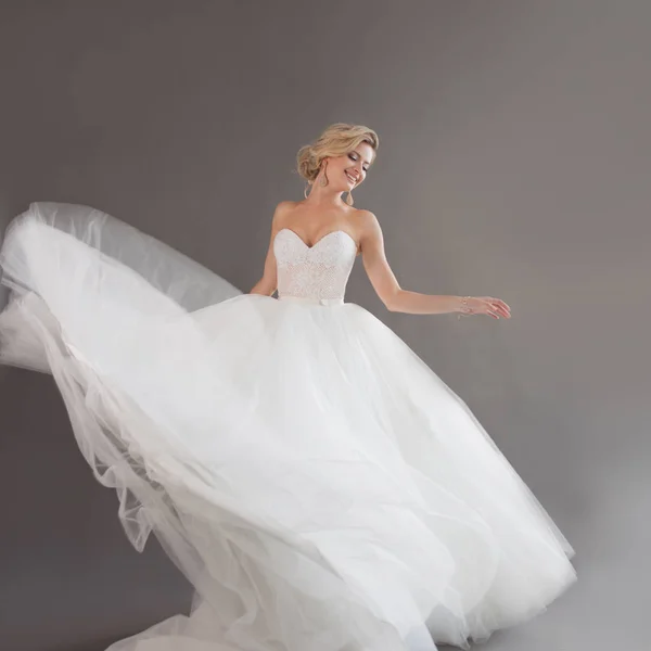 Dançando noiva jovem em vestido de noiva de luxo. Menina bonita de branco. Emoções de felicidade, riso e sorriso, fundo cinza — Fotografia de Stock