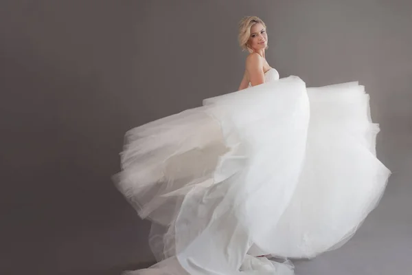 Dançando noiva jovem em vestido de noiva de luxo. Menina bonita de branco. Emoções de felicidade, riso e sorriso, fundo cinza — Fotografia de Stock