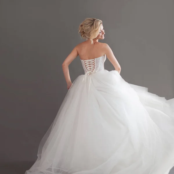 Bailando joven novia en lujoso vestido de novia. Una chica guapa de blanco. Emociones de felicidad, risa y sonrisa, fondo gris — Foto de Stock