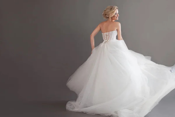 Tanzende junge Braut im luxuriösen Hochzeitskleid. hübsches Mädchen in Weiß. Glücksgefühle, Lachen und Lächeln, grauer Hintergrund — Stockfoto