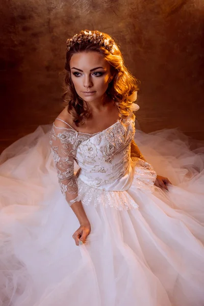 美丽的女孩新娘在奢华的婚礼礼服坐在地板，画像中的金色调，眩光的影响 — 图库照片