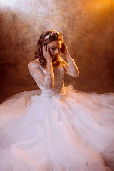 Beautiful girl bride in luxurious wedding dress sitting on the floor, portrait in Golden tones, effects of glare