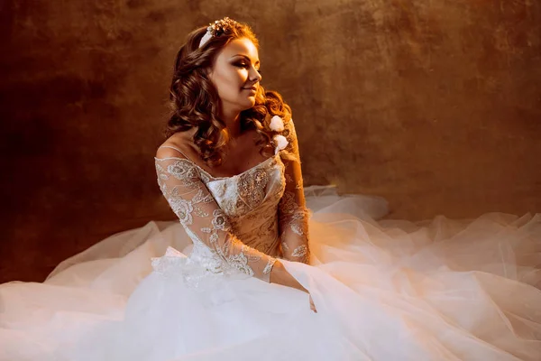 Mooi meisje bruid in luxe trouwjurk zittend op de vloer, portret in gouden tinten, effecten van glare — Stockfoto