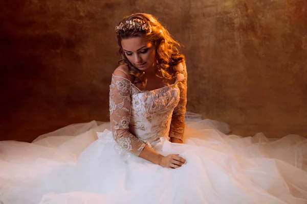 Hermosa novia chica en lujoso vestido de novia sentado en el suelo, retrato en tonos dorados, efectos de deslumbramiento —  Fotos de Stock