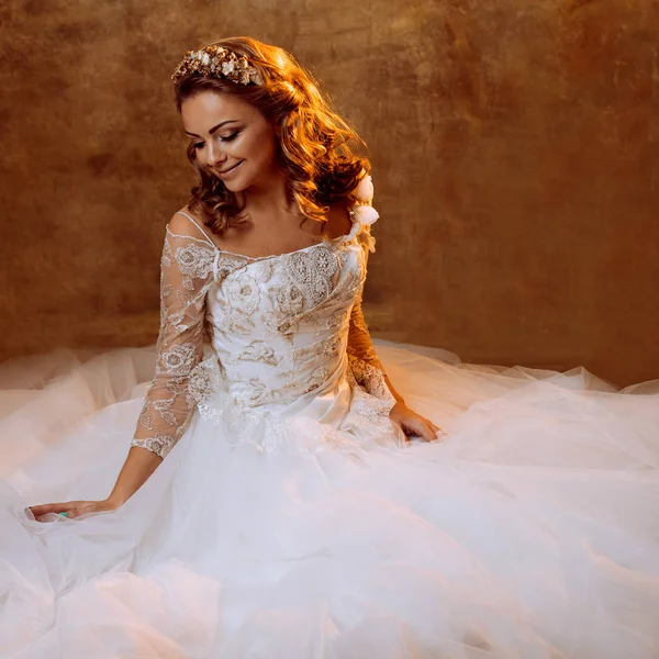 Hermosa novia chica en lujoso vestido de novia sentado en el suelo, retrato en tonos dorados, efectos de deslumbramiento — Foto de Stock