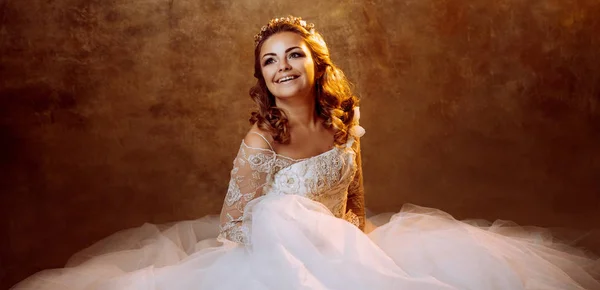 Erg blij meisje bruid in luxe trouwjurk zittend op de vloer, portret in gouden tinten — Stockfoto