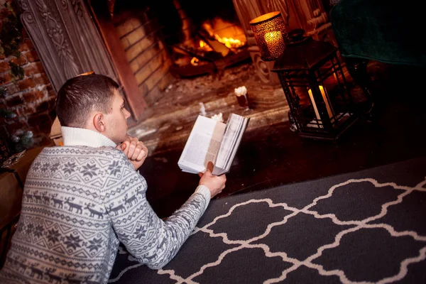 Ο άνθρωπος αναπαύεται δίπλα στο τζάκι, διαβάζοντας ένα βιβλίο στο σπίτι — Φωτογραφία Αρχείου