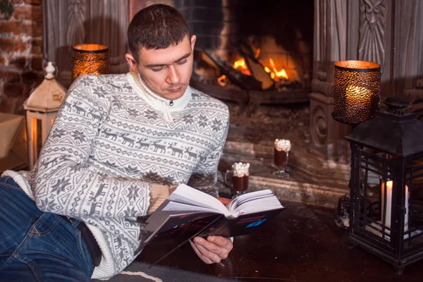 Man resting by the fireplace reading a book at home. Looking at the book