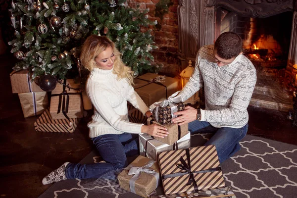 Pareja joven examina los regalos bajo el árbol de Navidad. Vacaciones —  Fotos de Stock