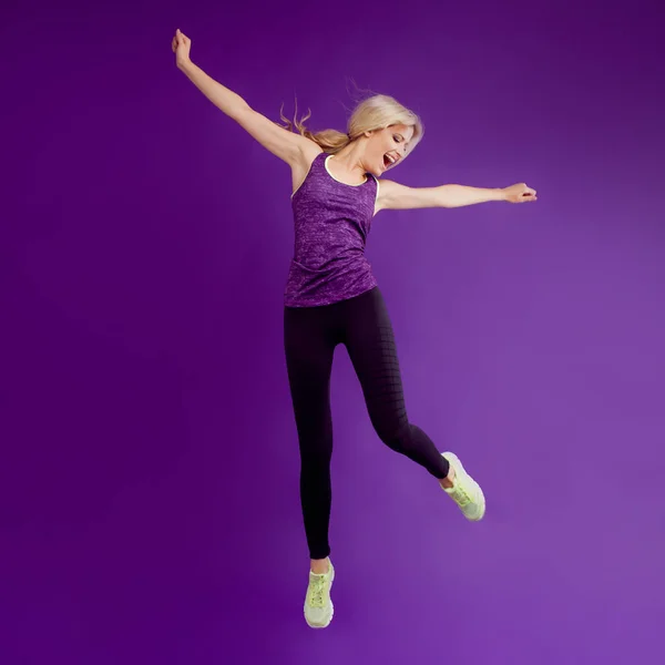 Vacker ung flicka i en pose löpare. Studio bakgrund, lila. Happy jumping — Stockfoto