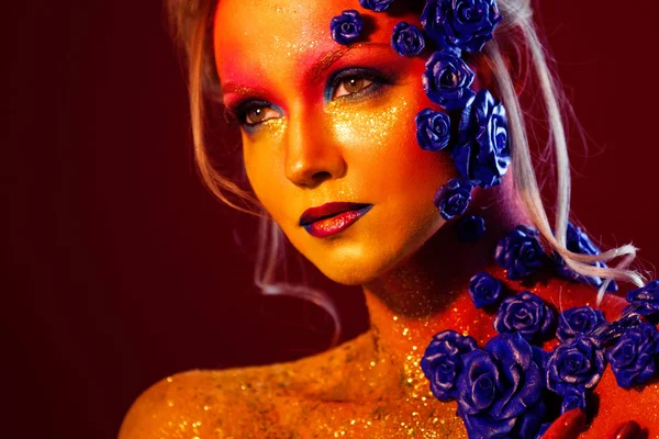 Portrait of young and attractive woman with art makeup. Fiery colors, glitter on face and floral decoration — Stock Photo, Image