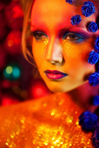 Porträtt av ung och attraktiv kvinna med konst makeup. Eldiga färger, glitter på ansikte och blomdekor — Stockfoto