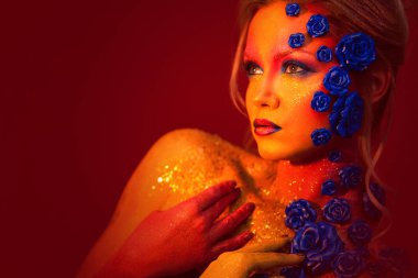 Sanat makyaj ile genç ve çekici bir kadın portresi. Ateşli renkler, parlak yüz ve çiçek dekorasyon