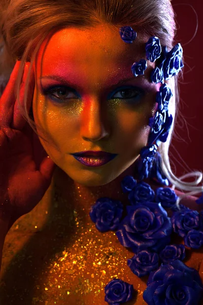 Portrét mladé a atraktivní žena s make-upem umění. Ohnivé barvy, třpytky na obličej a květinové dekorace — Stock fotografie