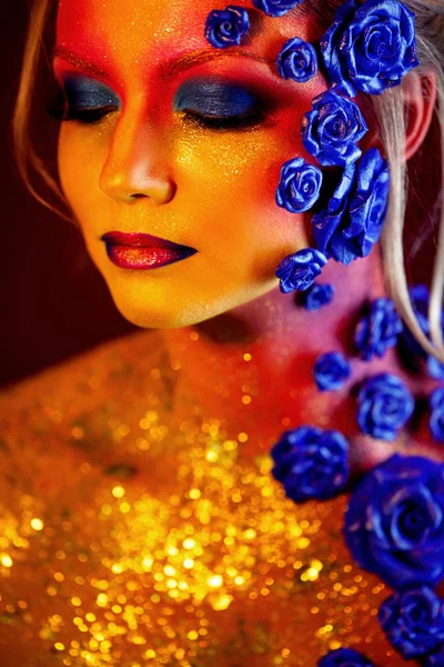 Retrato de mujer joven y atractiva con maquillaje artístico. Colores ardientes, brillo en la cara y decoración floral — Foto de Stock