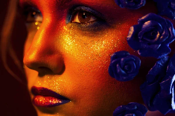Portret van jonge, aantrekkelijke vrouw met kunst make-up. Vurige kleuren, glitter op gezicht en florale decoratie — Stockfoto