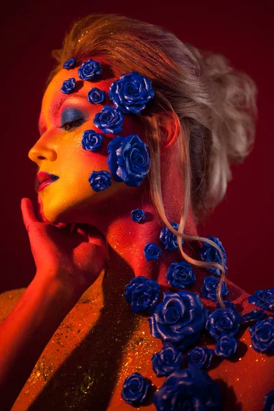 Porträtt av ung och attraktiv kvinna med konst makeup. Eldiga färger, glitter på ansikte och blomdekor — Stockfoto