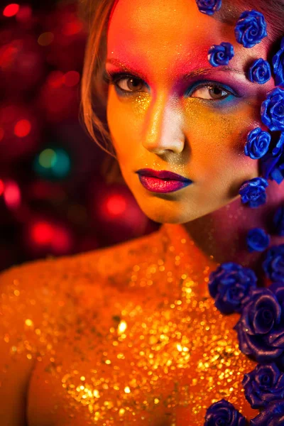 Retrato de mujer joven y atractiva con maquillaje artístico. Colores ardientes, brillo en la cara y decoración floral — Foto de Stock