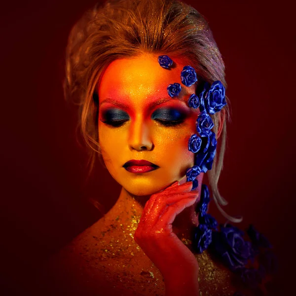 Porträtt av ung och attraktiv kvinna med konst makeup. Eldiga färger, glitter på ansikte och blomdekor — Stockfoto