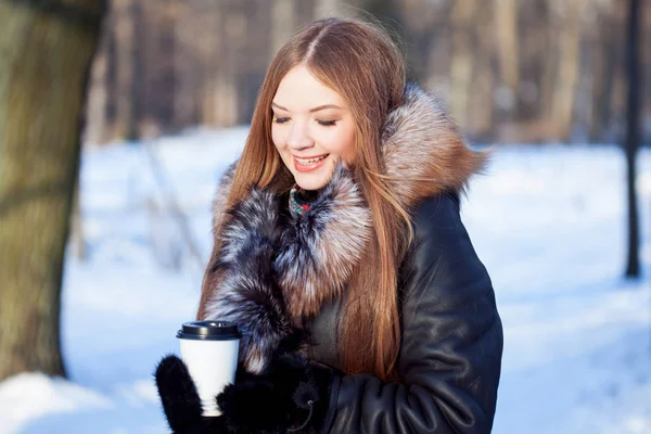 Femme jeune et séduisante à pied, hiver, manteau chaud avec capuche, café à emporter — Photo