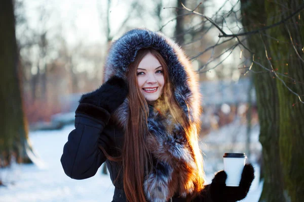 Femme jeune et séduisante à pied, hiver, manteau chaud avec capuche, café à emporter — Photo