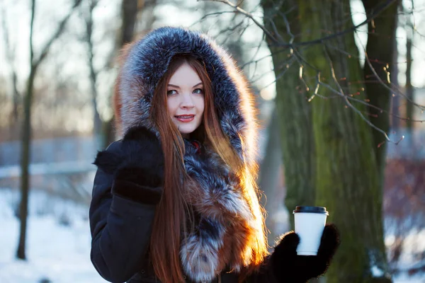 Femme jeune et séduisante à pied, hiver, manteau chaud avec capuche, café à emporter — Photo