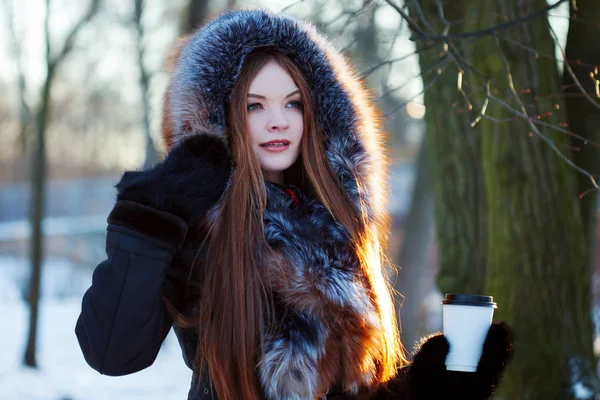 Femme jeune et séduisante à pied, hiver, manteau chaud avec capuche, café à emporter — Photo