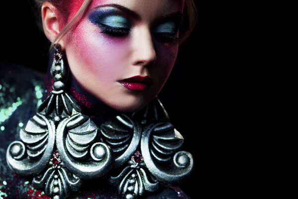 Young attractive blonde girl in bright art-makeup, high hair, body painting. Rhinestones and glitter
