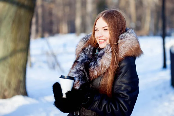 Femme jeune et séduisante à pied, hiver, manteau chaud avec capuche, café à emporter — Photo