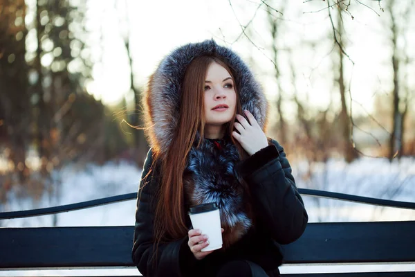 Молода і приваблива жінка на прогулянці, зима, тепле пальто з капюшоном, кава, щоб піти — стокове фото