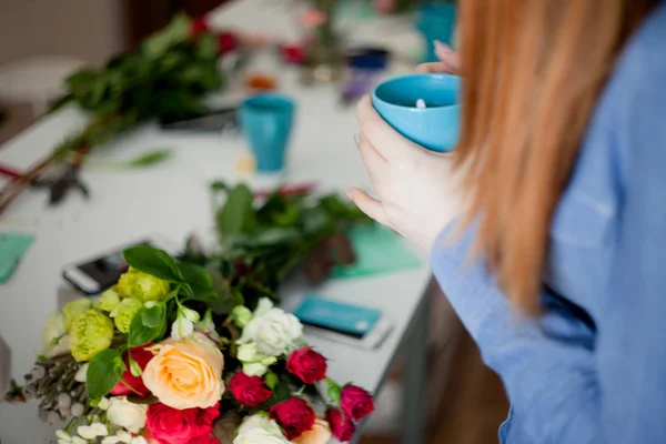 Florista de taller, haciendo ramos y arreglos florales. Mujer descansando con una taza de té en las manos. Enfoque suave — Foto de Stock