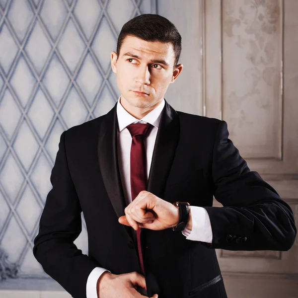 Young man in a tuxedo with tie. He looks at his watch