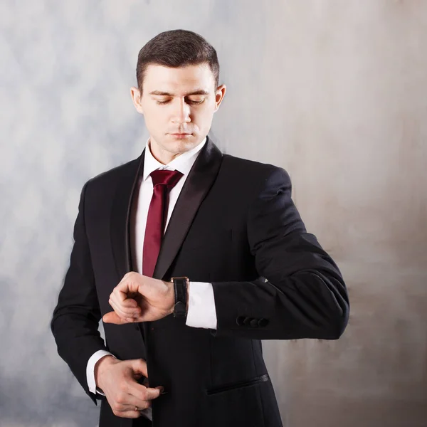 Jonge man in een smoking met stropdas. Hij kijkt op zijn horloge — Stockfoto