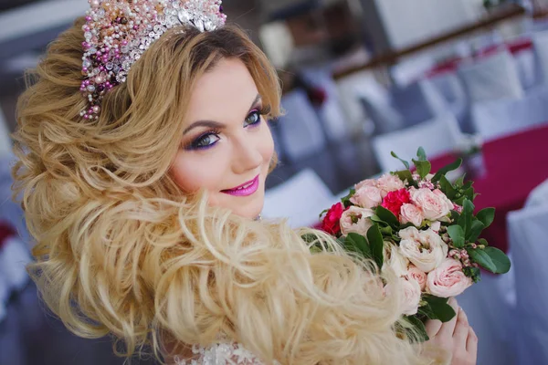 Jonge bruid met perfecte huid mode en make-up, krullend haar, bloemen en tiara op het hoofd, binnenshuis — Stockfoto