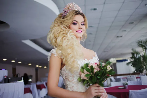 Jonge bruid met perfecte huid mode en make-up, krullend haar, bloemen en tiara op het hoofd, binnenshuis — Stockfoto