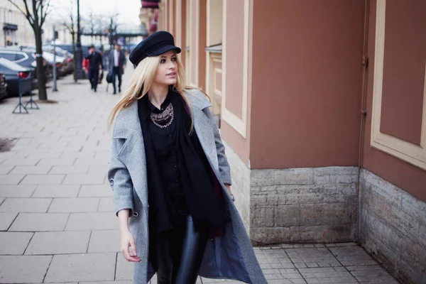 Молодая, модная и привлекательная блондинка гуляет по городу, девушка в стильной шляпе и сером пальто — стоковое фото