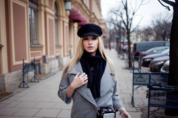 Joven, cadera y atractiva rubia paseando por la ciudad, chica con un sombrero elegante y un abrigo gris — Foto de Stock