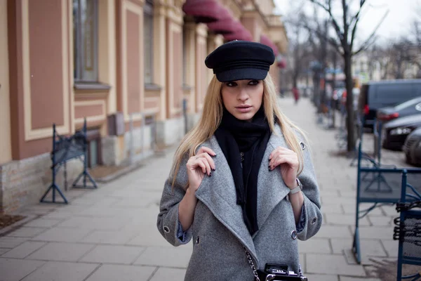 Молодая, модная и привлекательная блондинка гуляет по городу, девушка в стильной шляпе и сером пальто — стоковое фото