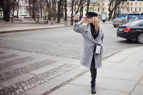 Молодая, модная и привлекательная блондинка, стоящая на пешеходном переходе, девушка в стильной шляпе и сером пальто — стоковое фото