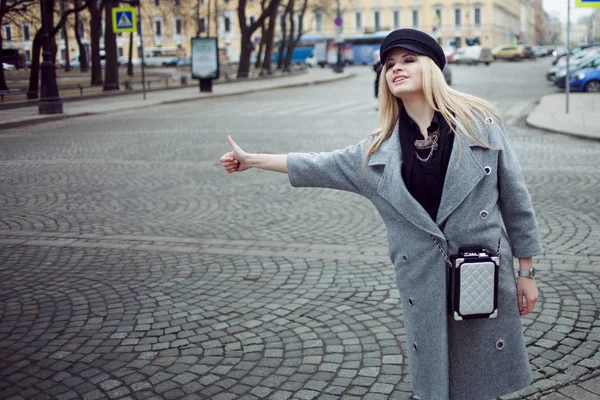 年轻、 髋关节和吸引力金发海陵出租车，在时尚的帽子和一件灰色的大衣的女孩 — 图库照片