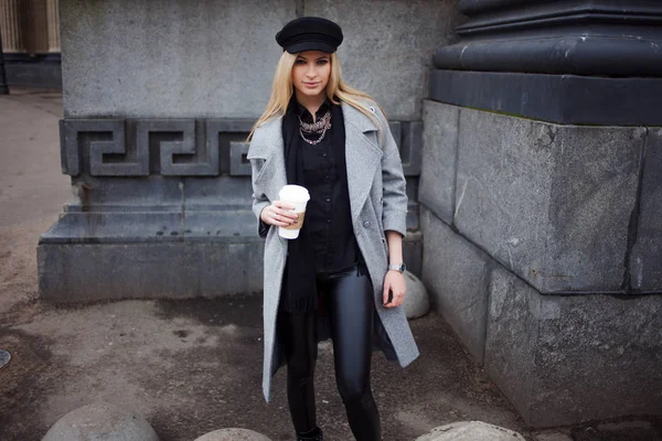 Jeune, branchée et jolie blonde se promène dans la ville avec du café à emporter, fille au chapeau élégant et manteau gris — Photo