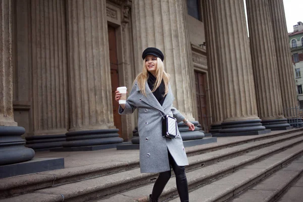 Junge, hippe und attraktive Blondine, die mit Coffee to go durch die Stadt läuft, auf die Uhr schaut und geschäftlich hastet — Stockfoto