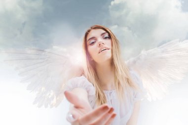 Gökten bir melek bir el verir. Beyaz kanatlı bir melek görüntüsündeki genç, harika sarışın kız.