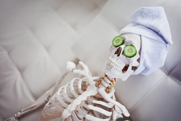 Skeleton in Spa salon with towel on her head and mask on her face, relaxes, care themselves. An absurd concept, social parody. Take care of beauty and forget about inner peace — Stock Photo, Image